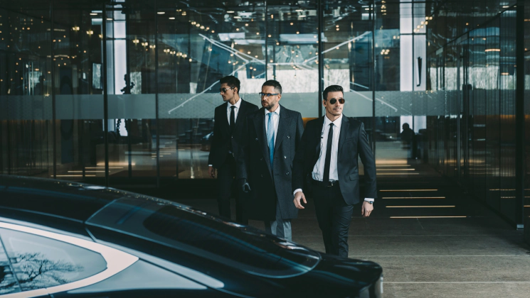 bodyguards with a a black suit and black sun glasses protecting a person